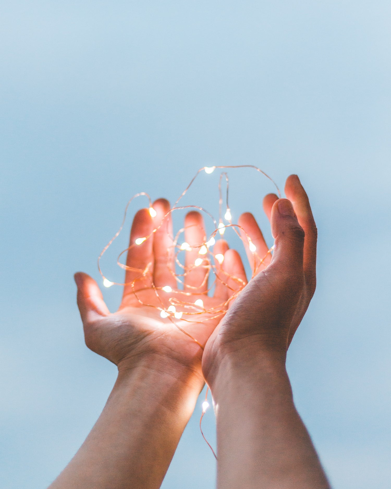 A person holds out their hands against a blue background and draws attention to a string of lights they hold in their palms.