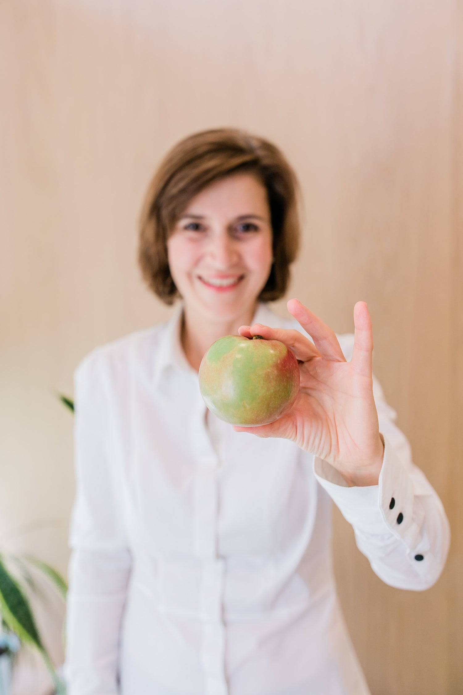 A brown-haired woman in a white shirt holds up an apple to encourage holistic health and nutrition