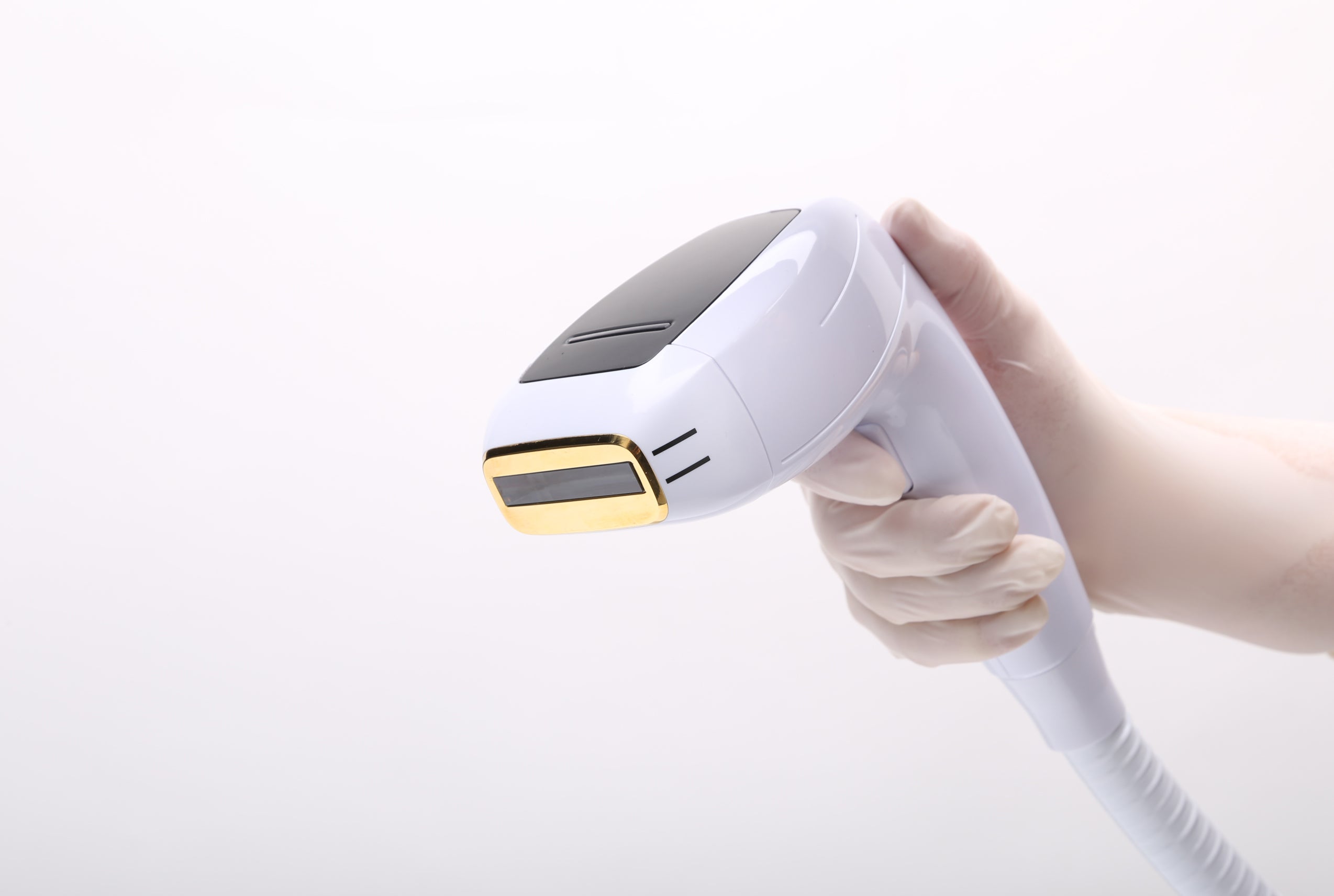 A laser hair removal tool is being held up by a person wearing latex gloves. This white and gold is used to remove hair and give patients silky smooth skin.