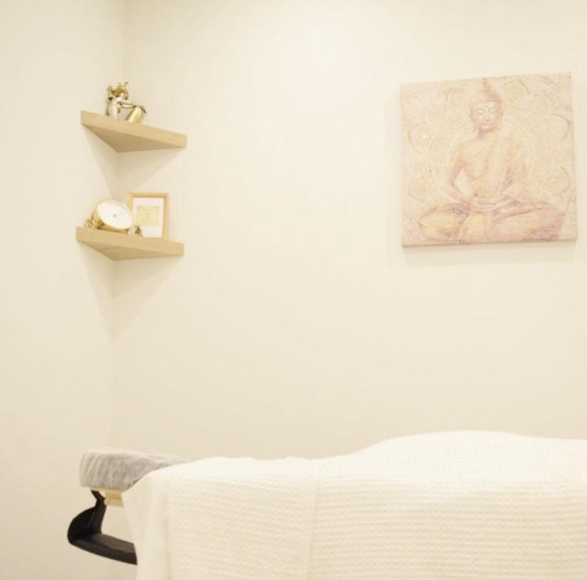 A massage table sits empty in a simply-decorated room. The table has a blanket laid across it in preparation for a prenatal massage therapy treatment.