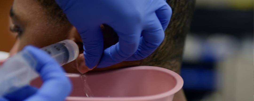 A person receives ear irrigation treatment to address their hearing loss concerns. A professional with blue gloves drains the patients ear into a pink catchment using a syringe.