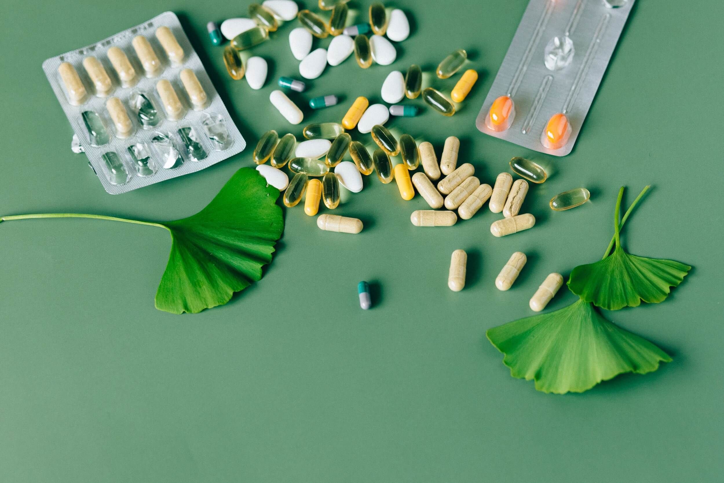 A vareity of supplements lay on a green table decorated with leaves